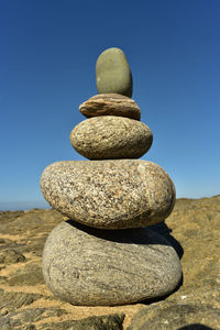 Stack of stones on rock against clear blue sky