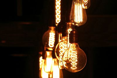 Low angle view of illuminated light bulbs hanging at night