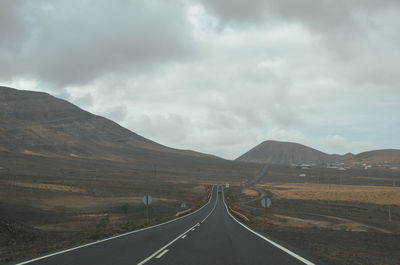 Empty road leading towards mountains against sky