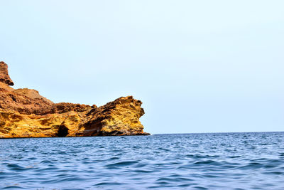 Rock formation in sea against clear sky