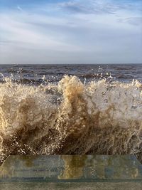 Sea waves splashing on shore against sky