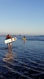 Men playing in sea against clear sky