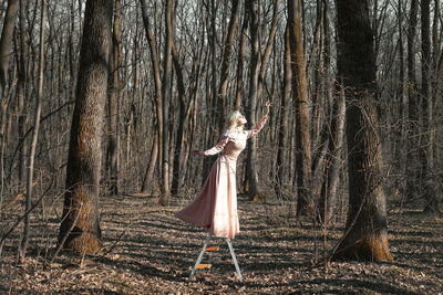 Woman in dress standing by tree trunk in forest
