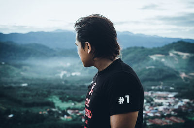 Young man looking at mountains against sky