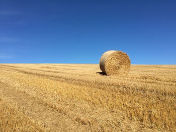 Hay bales on field against clear blue sky