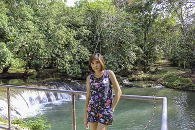 Portrait of beautiful woman standing with stream and trees in background