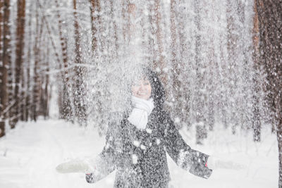 Smiling woman throwing snow mid air during winter