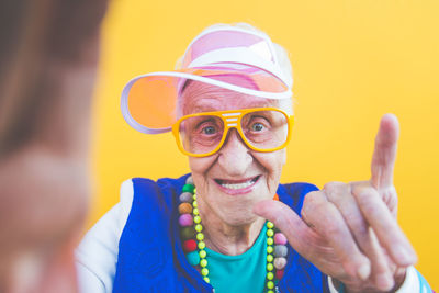 Portrait of senior woman wearing colorful jewelry standing against yellow background