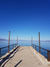 Pier on sea against clear blue sky