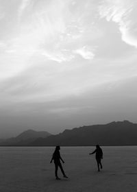 Silhouette people on sea by mountains against sky
