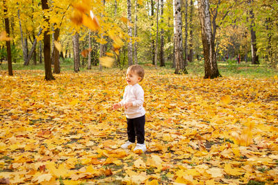 Full length of girl standing by yellow leaves during autumn