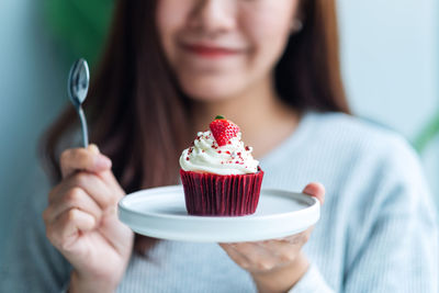 A beautiful asian woman holding a red velvet cupcake and spoon