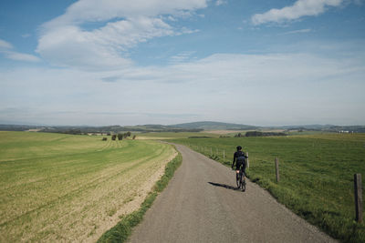 Rear view of man walking on field against sky