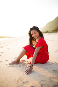 Portrait of happy woman sitting on beach against clear sky