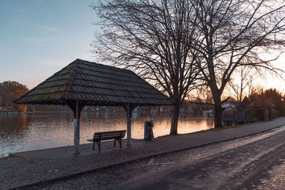 Empty bench by bare tree against sky during sunrise 