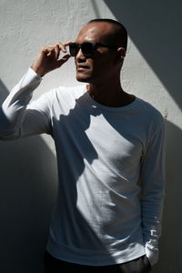 Young man wearing sunglasses standing against wall