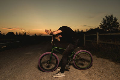 Man riding bicycle on field against sky during sunset