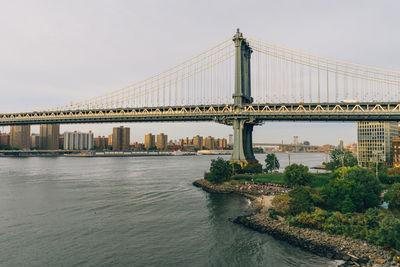 Suspension bridge over river against sky in city