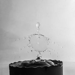 Close-up of drop splashing on water against white background