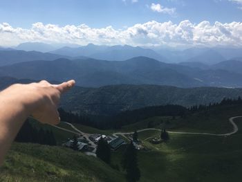 Cropped hand of person gesturing at mountain range against sky