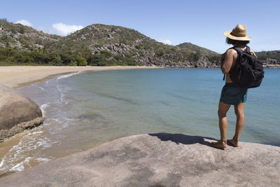 Man standing on rock by sea against mountain