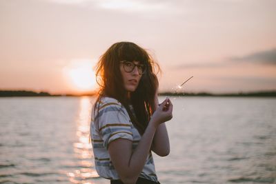 Beautiful woman standing by lake against sky during sunset