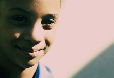 Close-up portrait of girl smiling against wall during sunny day