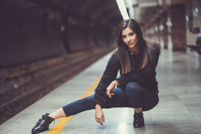 Portrait of beautiful woman crouching at railway station