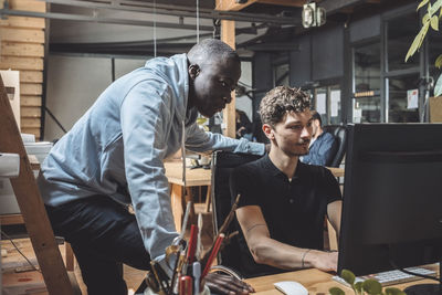 Businessman by colleague working on computer at workplace