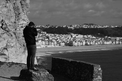 Rear view of man standing on rock against sky