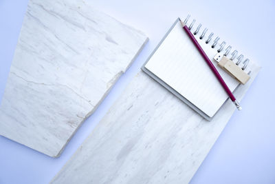 High angle view of spiral notebook with usb stick and pencil on marble over white background