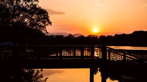 Silhouette trees by lake against sky during sunset