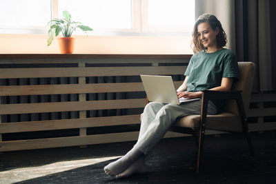 Young woman using laptop while sitting on chair at home