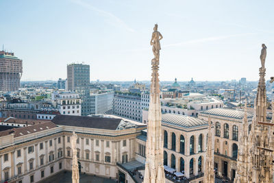 White statue on top of duomo cathedral and view to city of milan