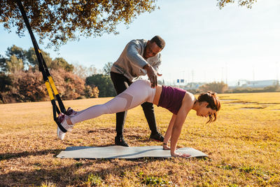 Full length of man assisting friend in exercising at public park