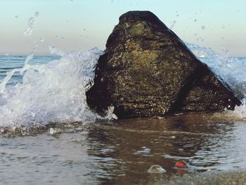 Sea waves splashing on rock against sky