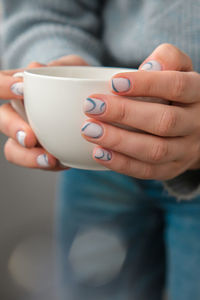 Manicured female hands holding white coffee cup with stylish blue nails and minimalistic design. 