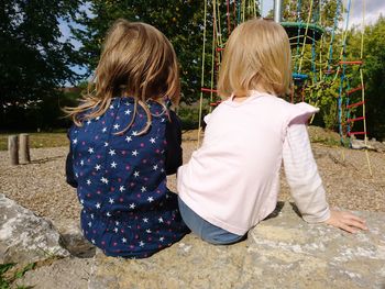 Rear view of siblings sitting on rock in playground