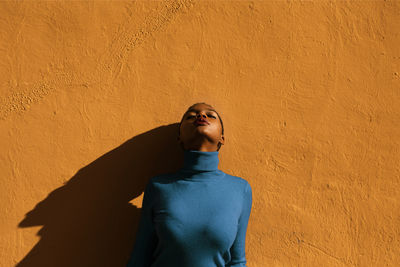 Portrait of african american young attractive woman in blue pullover leaning on orange background with closed eyes on a sunny day