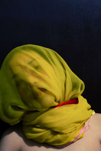 Close-up portrait of woman with face covered by yellow scarf against black background