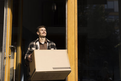 Contemplative man carrying box while leaving from apartment building