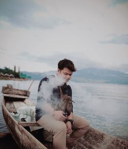 Young man sitting in sea against sky