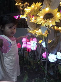 Rear view of girl standing by illuminated flowering plants