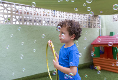 4-5 year old caucasian boy with curly hair in the backyard playing with soap bubbles