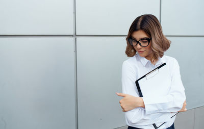 Young businesswoman with clipboard standing outdoors