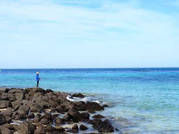 Man standing on rocks at sea against sky