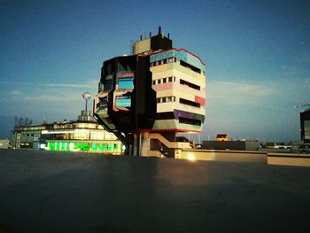 Building by illuminated city against sky at dusk