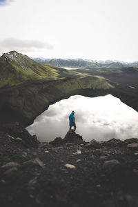 Rear view of man standing on rock by lake against sky