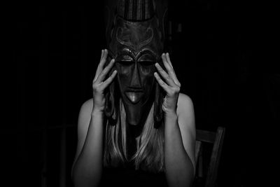 Woman covering face with mask against black background