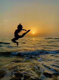 Silhouette woman jumping in sea against sky during sunset